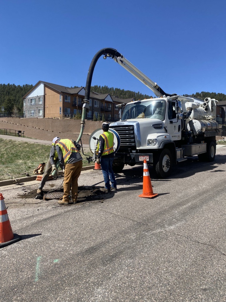 Collections and Distribution crew using hydro excavating to clean a sewer line.  Crews are in the road with a big truck that has a hose on it to flush the sewer line with high pressure water.