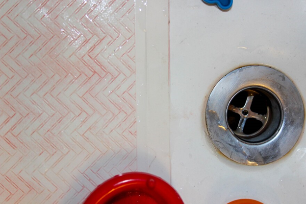 Picture of the bottom of a shower with pink substance in the grooves of the shower.